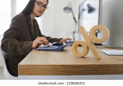 Corporate tax and interest rate. Close up of wooden percent sign standing on table on background of serious busy woman counting on calculator. Concept of interest calculation. - Shutterstock ID 2138286315