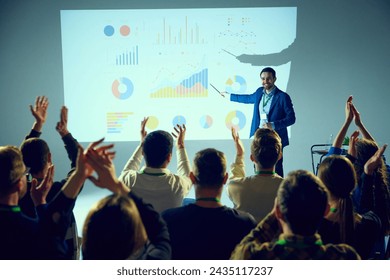 Corporate training lecture surrounded by data visualizations where man ending speech and audience clapping raising hands. Concept of business, startup, leadership and personal development courses. - Powered by Shutterstock