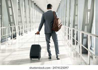 A corporate traveler with luggage is seen at an airport. The mood is focused and professional, with a modern airport setting that emphasizes travel and business, back view - Powered by Shutterstock