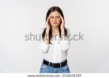 Corporate woman grimacing, touching head, feeling headache, severe migraine, standing over white background
