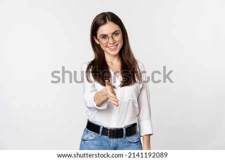 Corporate woman in office extending hand and smiling, handshake, greeting business partner, standing in glasses over white background