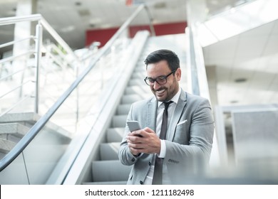 Corporate worker smiling and  using smart phone for writting message while going down the escalator.