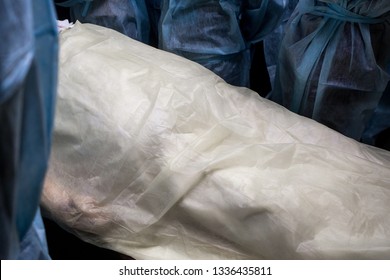 Corpse covered with cellophane surrounded by medical workers. The body of a man before the autopsy.