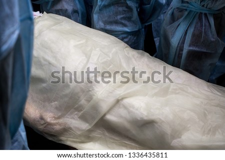 Corpse covered with cellophane surrounded by medical workers. The body of a man before the autopsy.