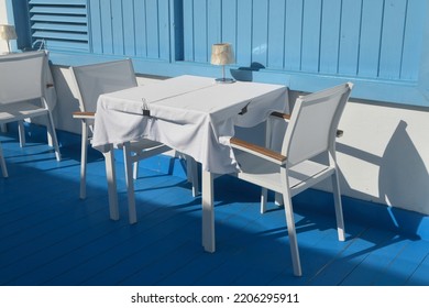 Corralejo, Fuerteventura, Spain: September 23 2022: White Table And Chairs With Blue Wooden Floor And Wall As Backdrop. Outdoors In Sunshine With Shadows. Restaurant, No People.