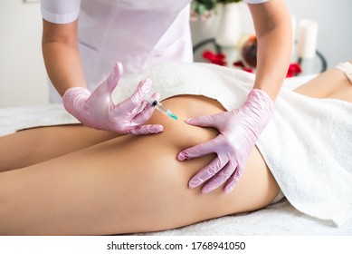 correction of body fat with lipolytics. in the cosmetologist s office, female hands in pink gloves inject a young woman in the thigh. white canvas. healthy body concept, slim body.
