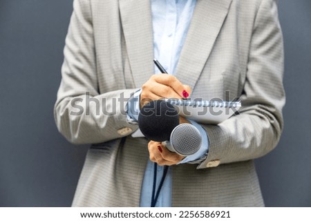 Correspondent or reporter at media event, holding microphone, writing notes. Journalism concept.