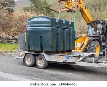 Corris, Gwynedd, Wales, UK.  March 30, 2022.   A JCB lifting an old oil tank and removing it from a house. 