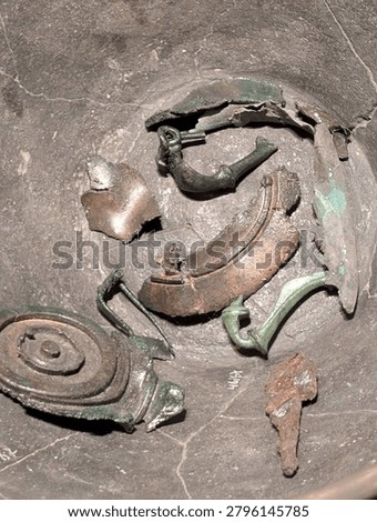 Corroded ancient bronze artifacts, including fibulae fragments, lie scattered, highlighting historical archaeological discoveries