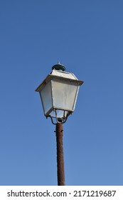 A Corroded Steel Street Lantern With Cloudy Glass Panels On A Brown Rusty Pole