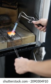 Cose-up of ceramic crucible with silver. Process of melting silver with gasoline burner. Male hands in frame. Jewelry Msterskaya. Inside oven hood. Blurred foreground.