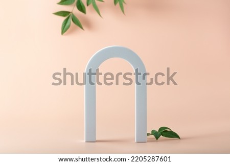 Cosmetic art deco arch display in pastel color for product presentation. Fashion geometric arch backdrop for product presentation and green leaves on pastel pink background. Abstract minimal template 