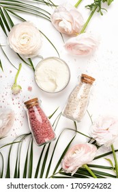 Cosmetic Body Or Face Cream Container And Bottle Of Bath Salts. Pastel Pink Ranunculus On White Marble Background, Flat Lay Or Top View