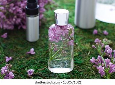 Cosmetic bottle close up with lilac flowers on the moss background
