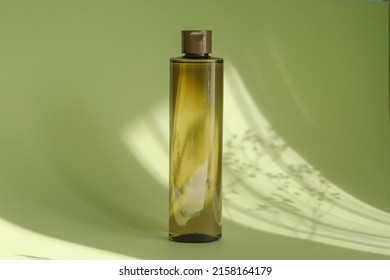 cosmetic bottle on green background with sunlight and floral shadow