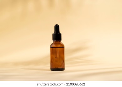 Cosmetic bottle with pipette. Brown liquid product in glass bottle with dropper. Serum skin care on light beige background and shadows. Beauty product mockup.