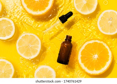 Cosmetic bottle product serum vitamin C with orange and lemon flat lay on yellow background clean water splashing, top view, copy space