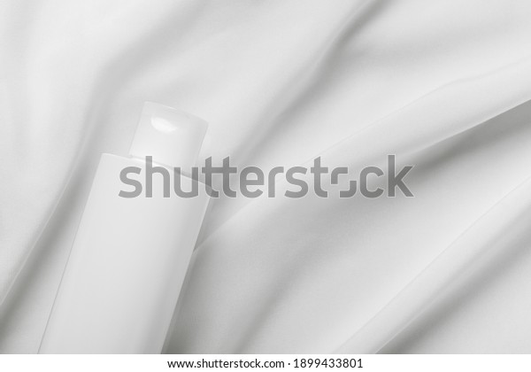 Cosmetic\
bottle tube packaging on white silk fabric background. Beauty and\
skincare concept, mockup for design. Minimal monochrome color\
composition. Top view, flat lay, copy\
space