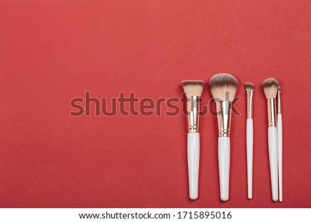 Cosmetic brushes in set lie on red juicy background, top view. Concept is work of makeup artist.