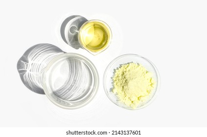 Cosmetic chemicals ingredient on white laboratory table. Sulfur Powder in Chemical Watch Glass and Poly Aluminium chloride liquid in beaker. Top View - Shutterstock ID 2143137601