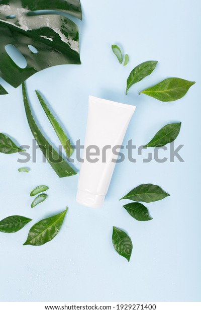 Cosmetic cream facial mockup tube
container or body lotion, aloe vera  and green leaves on blue
background. Natural cosmetic product concept, top view, copy
space.