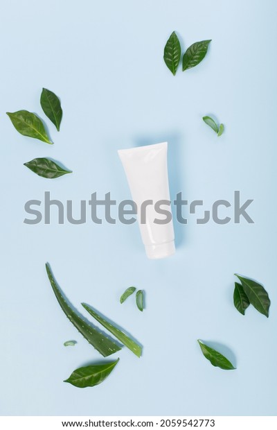 Cosmetic cream facial mockup tube\
container or body lotion, aloe vera  and green leaves on blue\
background. Natural cosmetic product concept, top view, copy\
space.