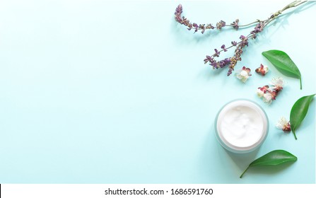 Cosmetic cream in a jar with green leaf and flowers on a light blue background. Concept natural cosmetics, aromatherapy, skincare. Top  view and copy space flay lay