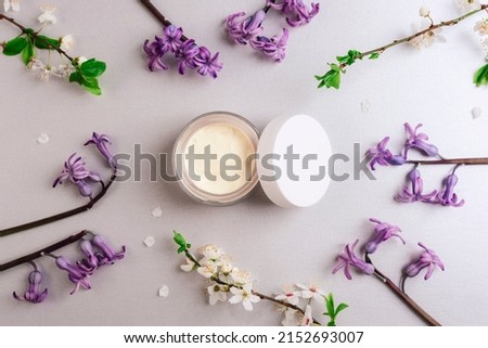 Cosmetic cream in a jar and spring blossom on light gray background. Natural cosmetics concept. Top view, flat lay.