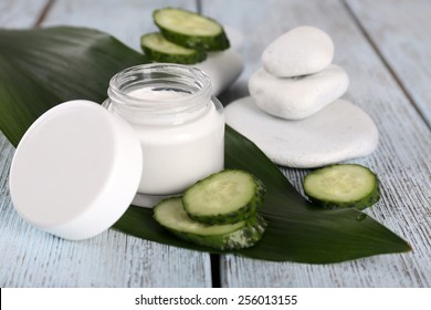 Cosmetic cream with slices of cucumber and spa stones on wooden background