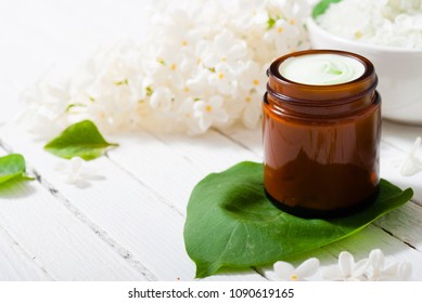 Cosmetic Creams And White Lilac Blossom On Bright Wooden Table Background