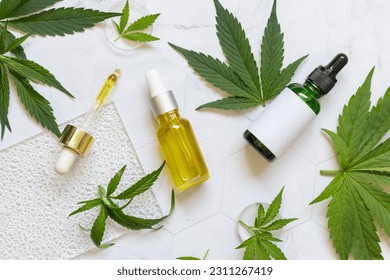 Cosmetic dropper bottles with blank label near green cannabis sativa leaves on a marble table top view. Mockup, Copy space. Organic skincare beauty products. Eco friendly CBD oil