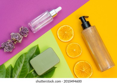 Cosmetic Flat Lay: Bronzer Body Glitter Cream, Face Serum, Craft Soap And Natural Elements On A Combination Of Backgrounds Green, Purple And Yellow Colours