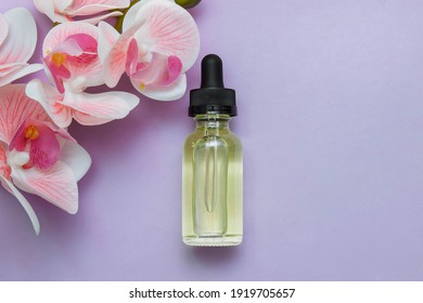 Cosmetic glass oil bottle with pipette on pink background with orchid flowers with empty space for text, closeup, skin care and treatment concept, facial vitamins, rejuvenation, acne and pimples