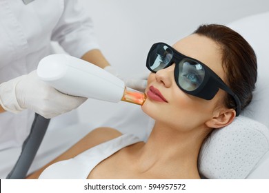 Cosmetic Laser Procedures. Beautician Uses Skin Resurfacing Equipment To Resurface Beautiful Woman Skin. Closeup Of Female  Receiving Beauty Treatment, Therapy. Body Care. High Resolution