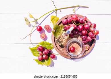 Cosmetic Oil, Whey Based On Grape Seed Oil In A Glass Vial With A Pipette On A Wooden Tray With A Bunch Of Grapes. Top View. White Wooden Background