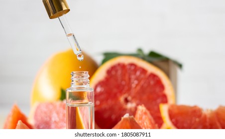 Cosmetic product, citrus essential oil in a glass bottle. Drop falling from a pipette. Against the background of grapefruit, orange