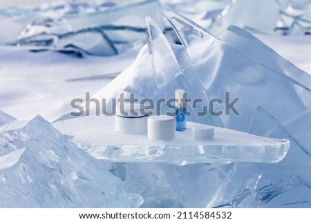 Cosmetic products for face and hand skin care in winter time. Advertising of nourishing cosmetics for cold weather on a podium stand from piece of ice against the backdrop of a frozen and snowy lake