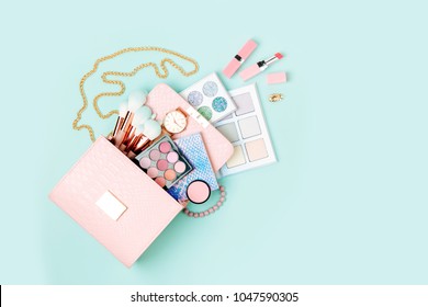 Cosmetic Products Flowing From Makeup Bag On Pastel Blue Background.  Flat Lay, Top View. Fashion Concept