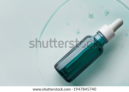 Cosmetic serum bottle sample on cold green gray background