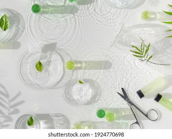 Cosmetic skincare background. Herbal medicine with green leaves. Natural sunlight, long shadows. Splashes of water, splashes. Chemical glassware, petri dishes, vials. Natural skincare background. - Shutterstock ID 1924770698