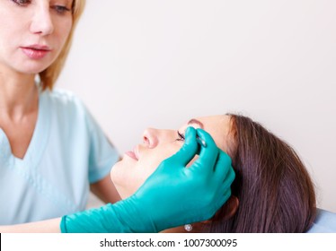 Cosmetic surgeon examining female client in office. Doctor checking woman's face, the eyelid before plastic surgery, blepharoplasty. Surgeon or beautician hands touching woman face. Rhinoplasty