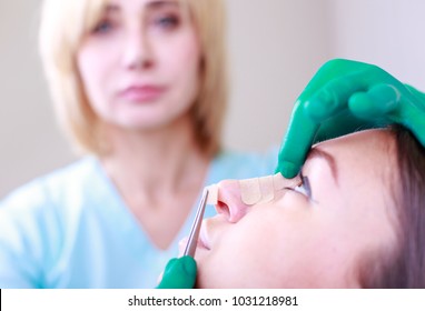 Cosmetic surgeon examining female client in office. Doctor checking woman's face, the nose after plastic surgery, Rhinoplasty . Surgeon or beautician hands touching woman face, makes bandaging.