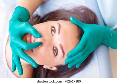 Cosmetic surgeon examining female client in office. Doctor checking woman's face, nose before plastic surgery. Surgeon or beautician hands touching woman face. Rhinoplasty