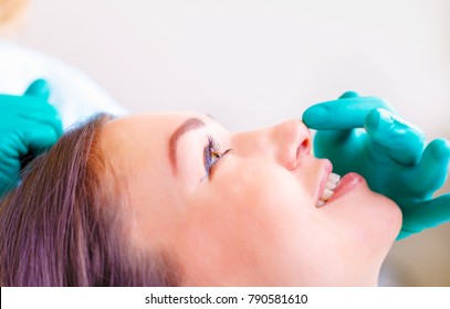 Cosmetic Surgeon Examining Female Client In Office. Doctor Checking Woman's Face, Nose Before Plastic Surgery. Surgeon Or Beautician Hands Touching Woman Face. Rhinoplasty