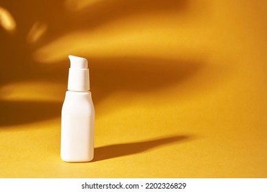 Cosmetic white bottle with a dispenser on a yellow background. The shadow of the monstera plant on the surface. Skin care. A container for cosmetic products for skin care. High quality photo