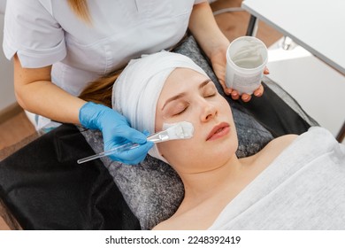 Cosmetician giving client facial skincare mask. Professional beautician provides comprehensive facial skin care for young woman. Pore cleansing procedures, all-season peeling, firming anti-aging mask. - Shutterstock ID 2248392419