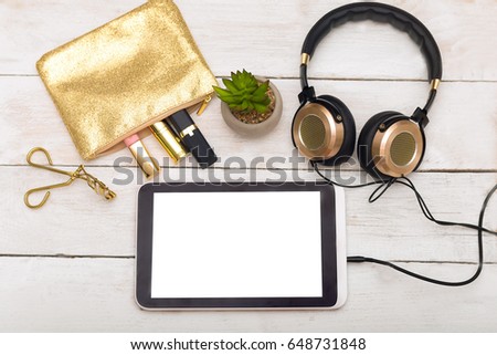 Cosmetics, gold headphones and gold cosmetic bag on a white wooden background