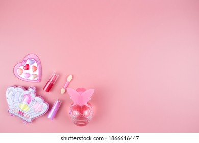 Cosmetics for little girls, baby perfume, lipstick, eye shadow, lip gloss, on a pink background.
