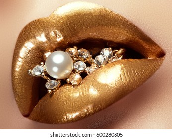 Cosmetics and make-up. Closeup of gold artistic lips. Glitter shiny lip makeup. Shoot of a beautiful girl with golden lipstick and gloss. Sexy and stylish lips. Pearls and diamonds in her mouth