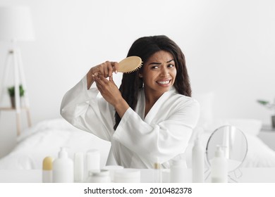 Cosmetics For Matted, Dry Hair, Treatment And Home Spa Therapy. Upset African American Woman Cannot Comb Curly Hair, Sitting In Bedroom Interior At Morning, Copy Space